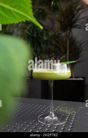 Glas mit grünem Matcha-Sour-Cocktail, verziert mit grünem Blatt auf dem Hintergrund und rosa Flovern Stockfoto