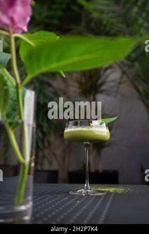 Glas mit grünem Matcha-Sour-Cocktail, verziert mit grünem Blatt auf dem Hintergrund und rosa Flovern Stockfoto