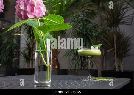 Glas mit grünem Matcha-Sour-Cocktail, verziert mit grünem Blatt auf dem Hintergrund und rosa Flovern Stockfoto