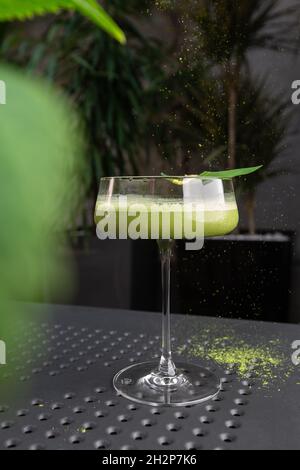 Glas mit grünem Matcha-Sour-Cocktail, verziert mit grünem Blatt auf dem Hintergrund und rosa Flovern Stockfoto