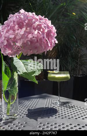 Glas mit grünem Matcha-Sour-Cocktail, verziert mit grünem Blatt auf dem Hintergrund und rosa Flovern Stockfoto