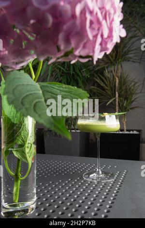 Glas mit grünem Matcha-Sour-Cocktail, verziert mit grünem Blatt auf dem Hintergrund und rosa Flovern Stockfoto