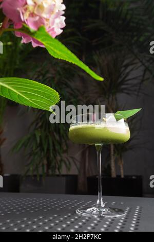 Glas mit grünem Matcha-Sour-Cocktail, verziert mit grünem Blatt auf dem Hintergrund und rosa Flovern Stockfoto