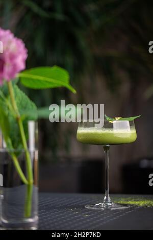 Glas mit grünem Matcha-Sour-Cocktail, verziert mit grünem Blatt auf dem Hintergrund und rosa Flovern Stockfoto