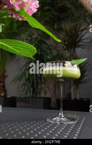 Glas mit grünem Matcha-Sour-Cocktail, verziert mit grünem Blatt auf dem Hintergrund und rosa Flovern Stockfoto