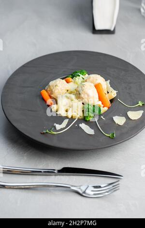 Teller mit Fleischbällchen mit weißer Sauce und Penne-Pasta, Baby-Karotte und Brokkoli. Grauer Steinhintergrund. Nahaufnahme. Draufsicht. Stockfoto