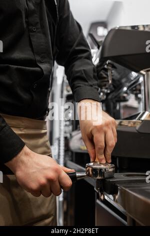 Der Prozess der Kaffee-Herstellung Schritt für Schritt. Mann stampfte frisch gemahlene Kaffeebohnen in einem Portafilter auf einem funktionierenden Holztisch Stockfoto