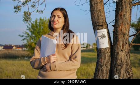 Besorgte Frau hält Papierstapel in der Nähe des fehlenden Katzenposters Stockfoto