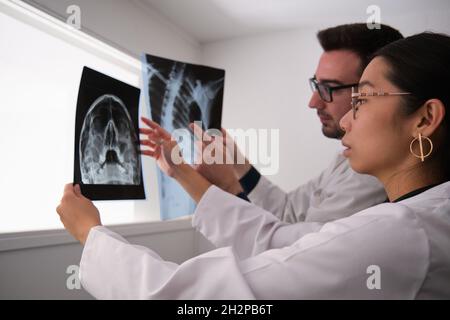 Zwei Ärzte, die einen Schädel und eine Rippe untersuchen, zeigen Röntgenbilder. Stockfoto