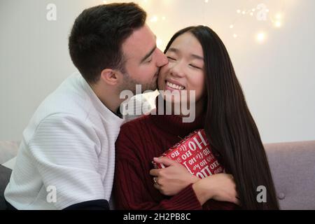 Romantisches junges multiethnisches Paar, das Weihnachtsgeschenke austauscht. Stockfoto