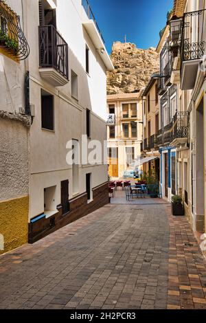 Schmale, historische Straße in Busot mit Blick auf den Hügel mit Burgruinen. Spanien in der Provinz Alicante.Vertikale Ansicht Stockfoto