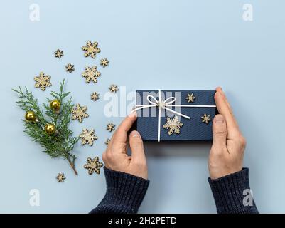 Mann Hände, halten Weihnachten oder Neujahr Geschenk auf blauem Hintergrund mit Feiertagsdekorationen. Flach liegend, Kopierplatz. Stockfoto