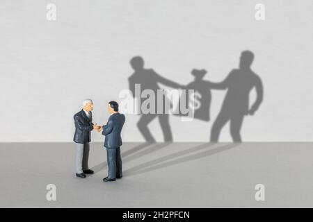 Gewinnbeteiligung. Zwei Geschäftsleute in Anzügen schütteln sich die Hände. SHADOW zwei Geschäftsleute nehmen sich einen Sack Geld von einander. Stockfoto