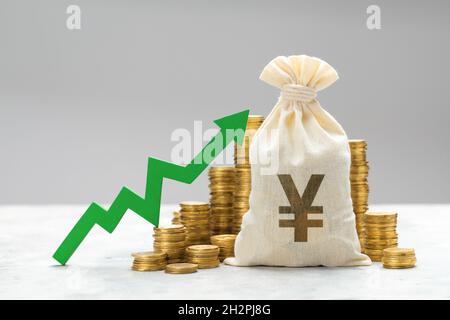 Grüner Pfeil auf dem Hintergrund der Münzen und eine Tasche mit dem YUAN-Symbol. Stockfoto