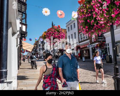 Guildford High Street mit einigen Einkäufern, die Covid-Gesichtsmasken tragen. Blumenkörbe im Herbst und farbenfrohe Banner der Saison in klarem, blauem, warmem Sonnenschein Stockfoto