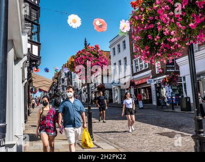 Guildford High Street mit einigen Einkäufern, die Covid-Gesichtsmasken tragen. Blumenkörbe im Herbst und farbenfrohe Banner der Saison in klarem, blauem, warmem Sonnenschein Stockfoto