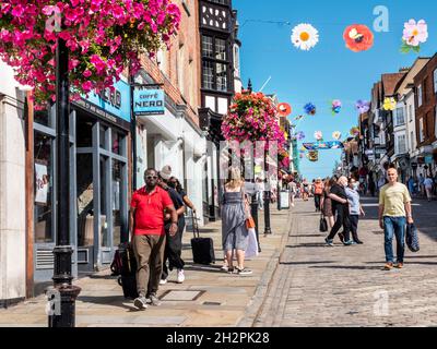 In der Guildford High Street gibt es Geschäfte mit Einkäufern, einige tragen Covid-Masken. Blumenkörbe im Herbst und farbenfrohe Banner der Saison in klarem, blauem, warmem Sonnenschein Stockfoto