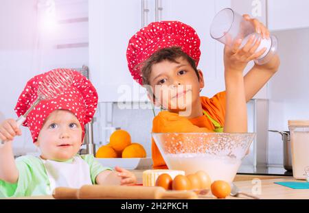 Junge fügen Sie Zucker zu mischen Schüssel machen Teig mit Bruder Stockfoto