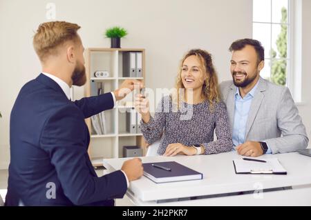 Immobilienmakler übergibt Schlüssel zu seinem neuen Zuhause an aufgeregt verheiratete Paar bei der Sitzung im Büro. Stockfoto