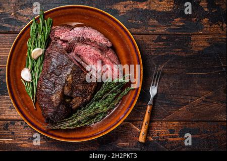Gerösteter Aufhänger oder Onglet-Rinderfleischsteak in Scheiben auf einem rustikalen Teller mit Hackschnitzel. Dunkler Holzhintergrund. Draufsicht. Speicherplatz kopieren Stockfoto
