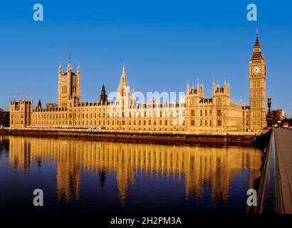 Parlamentsgebäude, die von klarem Sonnenaufgang beleuchtet werden, spiegeln sich bei Flut von Westminster Bridge London in der Still River Thames wider Stockfoto