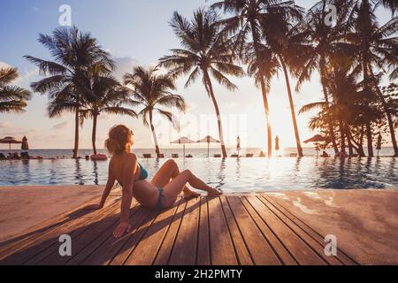 Tropisches Refugium im luxuriösen Strandhotel, Luxusreise, Frau, die sich bei Sonnenuntergang am Pool entspannt Stockfoto