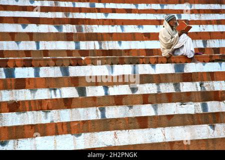 INDIEN. EIN BUCH IN DER HAND, EIN MANN BETET VOR DEM GANGES AUF DEN STUFEN VON KEDAR GHAT IN VARANASI (BENARES) Stockfoto