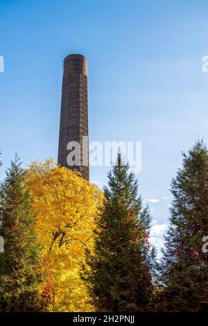 Alter, gemauerter Fabrikschornstein in der ehemaligen Kohlebergwerk 'Michal' in Siemianowice, Schlesien, Polen. Blauer Himmel im Hintergrund, Herbstbäume im Vordergrund. Stockfoto