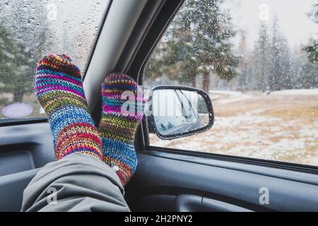 Gemütliche Reisezeit auf Roadtrip, Füße in bunten Socken im Auto am regnerischen Herbsttag Stockfoto