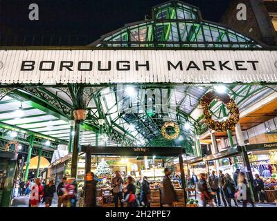 WEIHNACHTSMARKT AM BOROUGH Festlicher Eingang am Borough Market, beleuchtet in der Nacht mit Weihnachtskränzen, beschäftigt mit nächtlichen Einkäufern, die an internationalen Marktständen für Erzeugnisse einkaufen, Southwark London Stockfoto