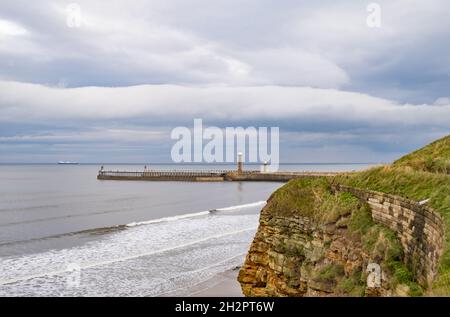 Ein entfernter Whitby West Pier oder Steg, der an einem trüben und bewölkten Herbsttag von den Klippen gefangen wurde Stockfoto