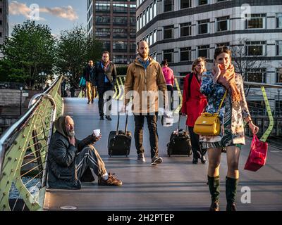 CITY WORKERS BETTELN CUP BETTLER CITY Canary Wharf London Workers smart gut gekleidet in öffentlichen Finanzämtern Bezirk, zu Fuß an sitzenden älteren Mann von untergehenden Sonne beleuchtet, appelliert für Bargeld mit seinem erweiterten Plastikbecher LONDON UK Stockfoto