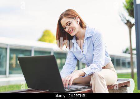 Junge beschäftigt Rotschopf freiberufliche Frau lachend während Online-Cummuncation im Park Stockfoto