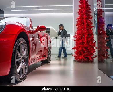 Ferrari Showroom zu Weihnachten, mit einem Jungen, der 12-14 Jahre auf seinem Smartphone war und auf den glänzenden Sportwagen Ferrari California schaute. Stockfoto