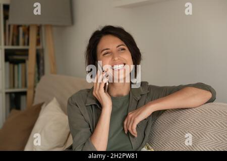 Fröhliche, aufgeregte Lateinerin, die während eines lustigen Telefongesprächs lacht Stockfoto