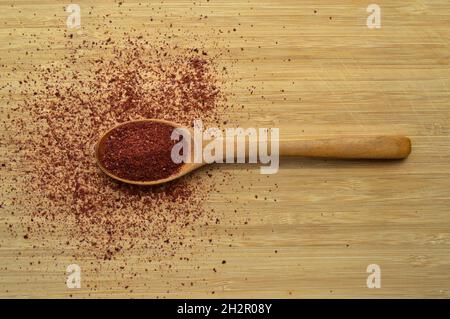 Gemahlene organische aromatische Sumac-Textur in Holzlöffel auf Bambus-Schneidebrett Stockfoto