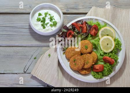 Vegetarische Falafel mit Salat auf einem Teller und Joghurt-Dip in einer Schüssel auf einem rustikalen grauen Holztisch, Kopierraum, Hochwinkel-Ansicht von oben, ausgewählte Focu Stockfoto