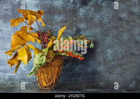 Herbst ikebana.Fall gelbe Kastanienblätter, Zweige mit wilden roten und orangefarbenen Beeren in einem Weidenkorb Stockfoto