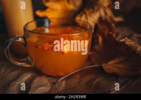 Nahaufnahme llarge Tasse heißen orange Sanddorn Tee in einem gemütlichen Hause Herbst Abend Stillleben mit trockenen Blättern. Stockfoto