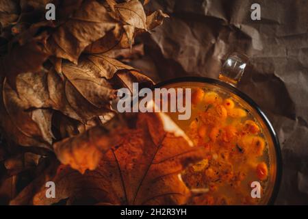 Nahaufnahme llarge Tasse heißen orange Sanddorn Tee in einem gemütlichen Hause Herbst Abend Stillleben mit trockenen Blättern. Stockfoto