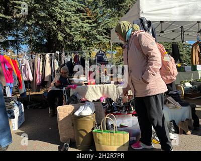 Frau, die mit Second-Hand-Kleidung und -Schuhen durch Flohmarktstände schlendert. Sie prüft die Waren und hat am sonnigen Oktobersamstag eine tolle Zeit. Stockfoto