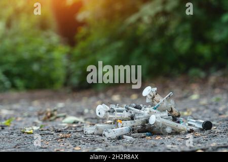 Ein Haufen von gebrauchten schmutzigen Spritzen, die nach der Medikamenteninjektion auf dem Boden im Freien lagen, war ausgezogen Stockfoto