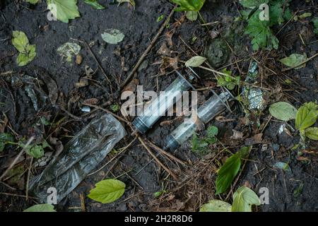 Ein Haufen von gebrauchten schmutzigen Spritzen, die nach der Medikamenteninjektion auf dem Boden im Freien lagen, war ausgezogen Stockfoto