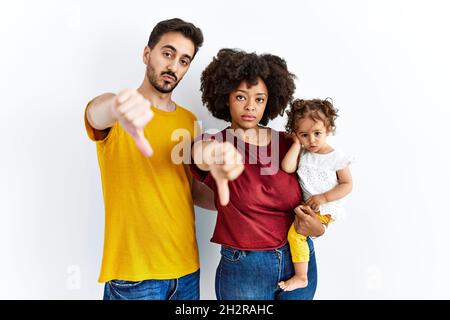 Gemischtrassig junge Familie von schwarzer Mutter und hispanischen Vater mit Tochter, die unglücklich und wütend aussagend Ablehnung und negativ mit Daumen nach unten g Stockfoto