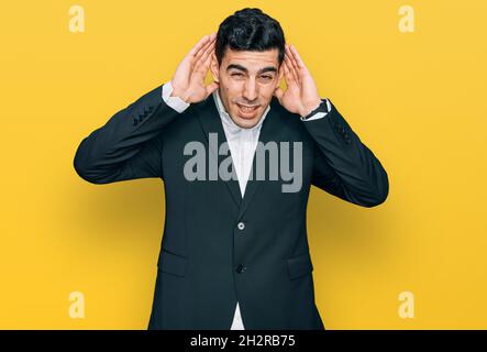 Gutaussehender hispanischer Mann in Geschäftskleidung versucht, beide Hände auf Ohr Geste zu hören, neugierig auf Klatsch. Hörproblem, taub Stockfoto