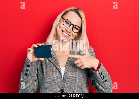 Schöne kaukasische blonde Geschäftsfrau hält ssd-Speicher lächelnd glücklich zeigt mit Hand und Finger Stockfoto