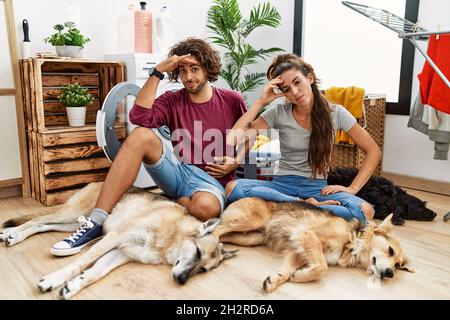 Junge hispanische Paar, die mit Hunden Wäsche waschen, besorgt und gestresst über ein Problem mit der Hand auf der Stirn, nervös und besorgt wegen einer Krise Stockfoto