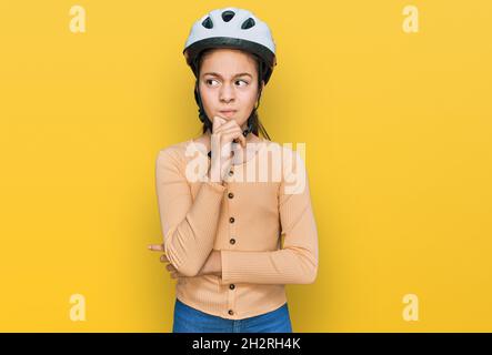 Schöne Brünette kleines Mädchen trägt Fahrradhelm ernstes Gesicht Denken über Frage mit der Hand auf dem Kinn, nachdenklich über verwirrende Idee Stockfoto