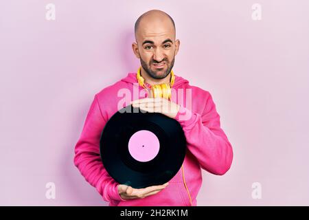 Junge Glatze Mann hält Vinyl-Disc ahnungslos und verwirrt Ausdruck. Zweifel Konzept. Stockfoto