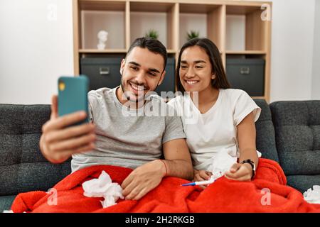 Junges lateinamerikanisches krankes Paar, das zu Hause eine medizinische Fernsultation mit dem Smartphone hat. Stockfoto